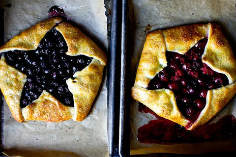 Two homemade star-shaped galettes filled with berries on a baking sheet featuring black and red fruits.