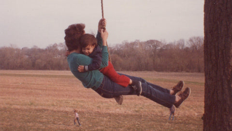 A parent and child enjoying a swing together in a scenic outdoor field.