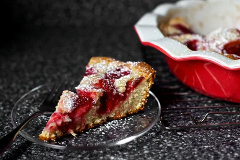 Delicious slice of berry cake with powdered sugar on a glass plate next to the baking dish.