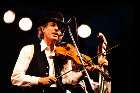 Musician performing on stage with a violin and microphone, illuminated by bright stage lights.