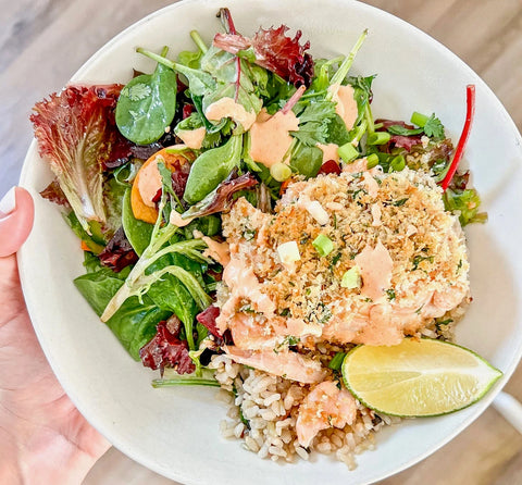 A healthy dish with baked salmon topped with herbs, served over brown rice and mixed greens, garnished with lime.