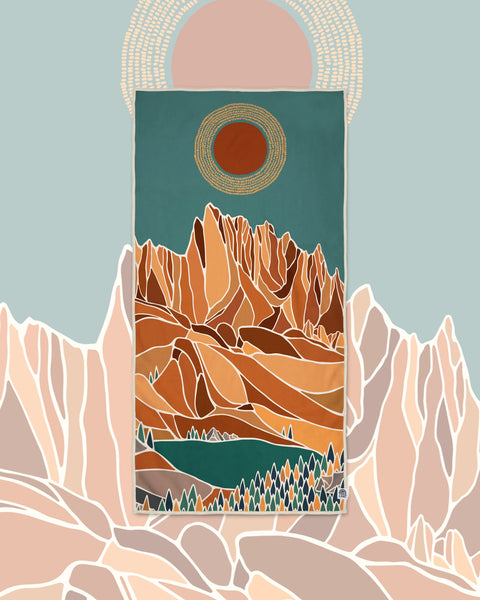 Alpenglow Wander & Travel Towel with orange and teal mountain lake print, set against pink peaks and a sun.