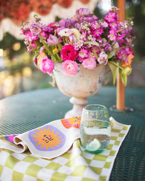 Always Sunny Kitchen & Tea Towel on a table with flowers and a glass of water.