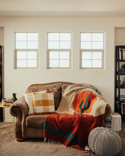 Cozy Trek Light Arizona Blanket on a couch, handwoven from recycled materials, featuring a desert sunset and cactus design. Beautiful and versatile.