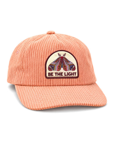 Be The Light Hat, a peach corduroy cap with a lightly curved brim and an embroidered moth patch reading "BE THE LIGHT," on white.
