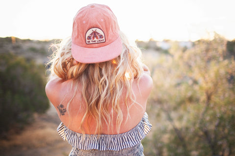 Woman wearing a Be The Light Hat, showcasing its stylish design and adjustable fit in a sunny outdoor setting.