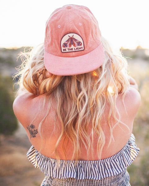 Woman wearing a Be The Light Hat, showcasing its stylish design and adjustable fit in a sunny outdoor setting.