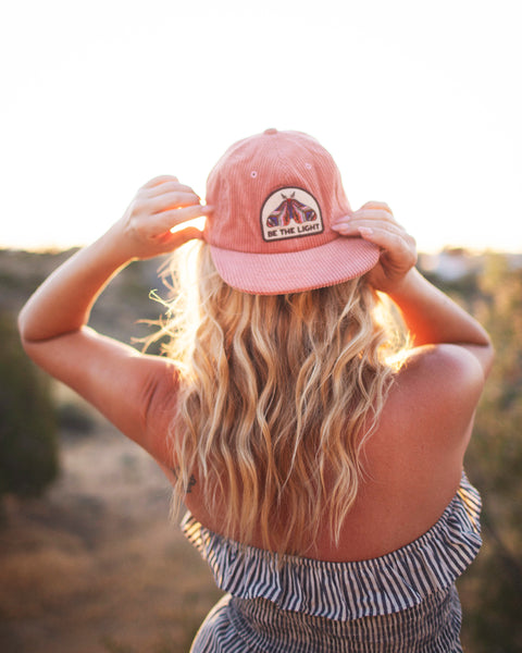 A woman wearing a Be The Light Hat, enjoying the outdoors during sunset, showcasing the hat's design and style.