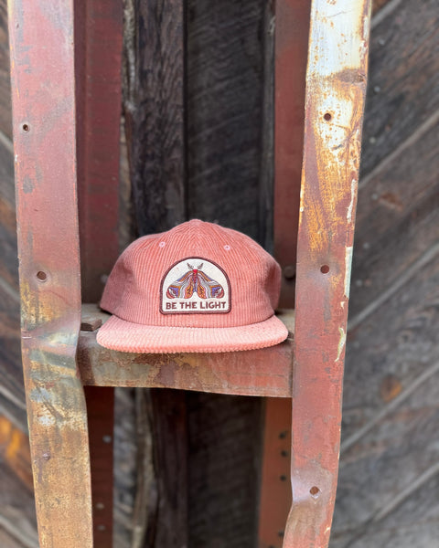 Be The Light Hat displayed on a rustic rack, showcasing its unique design and message.