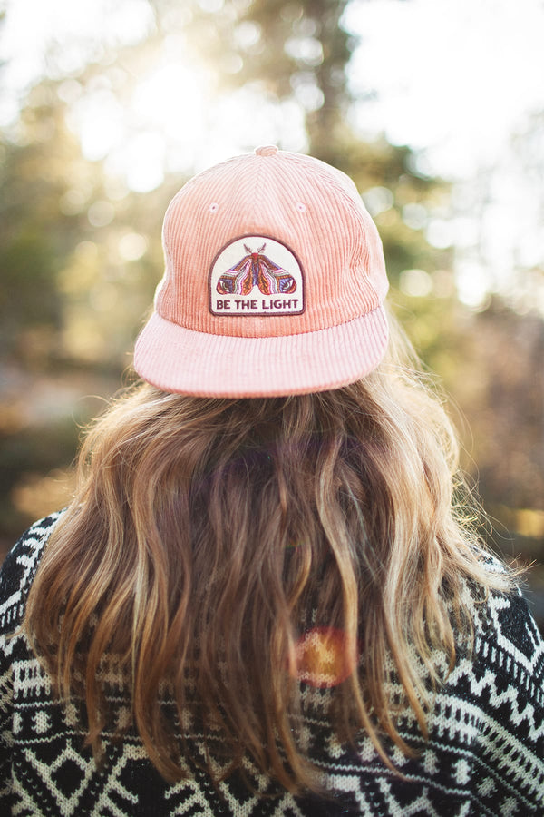 Be The Light hat with painted moth design, 6-panel snapback, flat brim, in a scenic outdoor setting. Trek Light style for all.