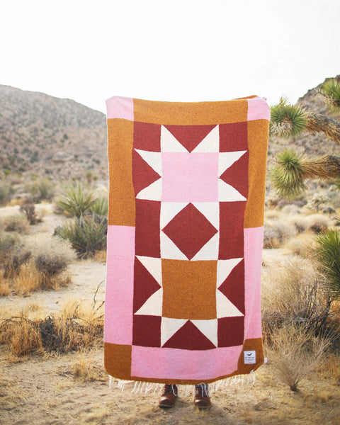 Person holding the Bernie Blanket outdoors, showcasing its vibrant design and midweight texture against a mountain backdrop.
