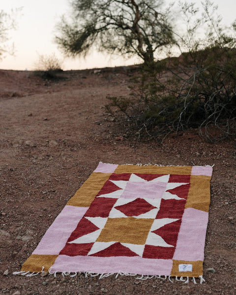 Beautiful handwoven Bernie Blanket made from recycled clothing, lying on desert ground, versatile and cozy. By Trek Light.
