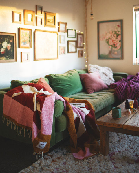 Cozy living room with the beautiful Bernie Blanket, handwoven using recycled clothing materials draped over a green sofa. By Trek Light.
