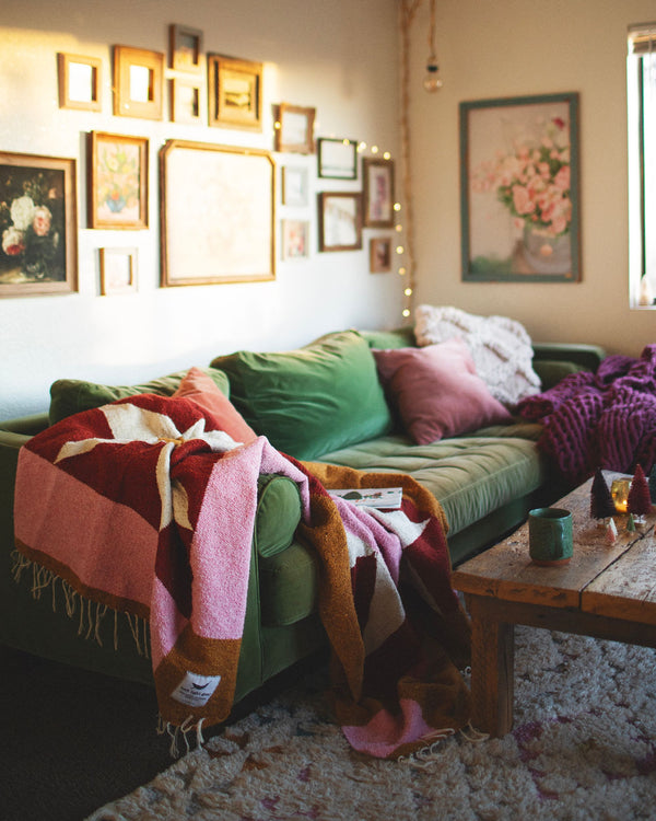 Cozy living room with the beautiful Bernie Blanket, handwoven using recycled clothing materials draped over a green sofa. By Trek Light.