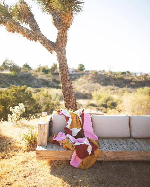Cozy Bernie Blanket draped on wooden couch in desert setting, perfect for outdoor relaxation.
