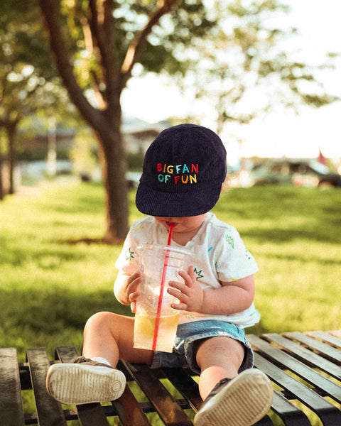 Toddler wearing Big Fan Of Fun Kids Hat while enjoying a drink on a sunny day outdoors.