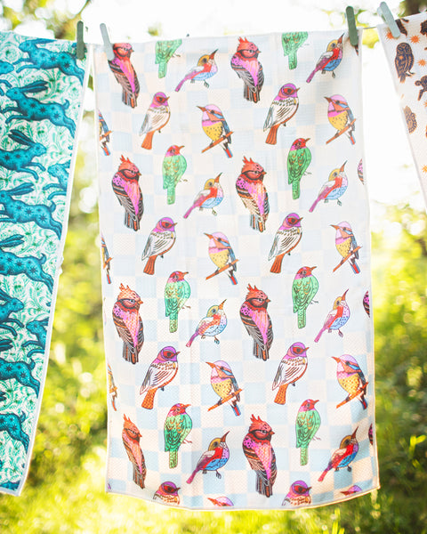 Bird Song Kitchen & Tea Towel hanging outside, featuring colorful birds on a vibrant background.