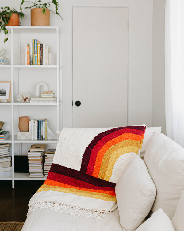 Cozy Trek Light Bowie Blanket draped on a sofa, showcasing vintage rainbow design for sustainable and stylish comfort.