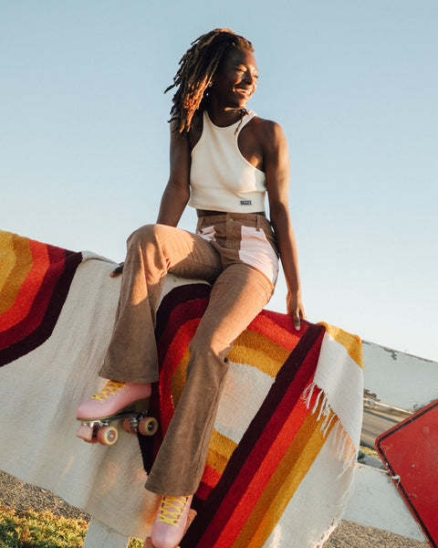 A woman on roller skates styled in a vintage vibe, enjoying the sun with a colorful Bowie Blanket draped behind her.