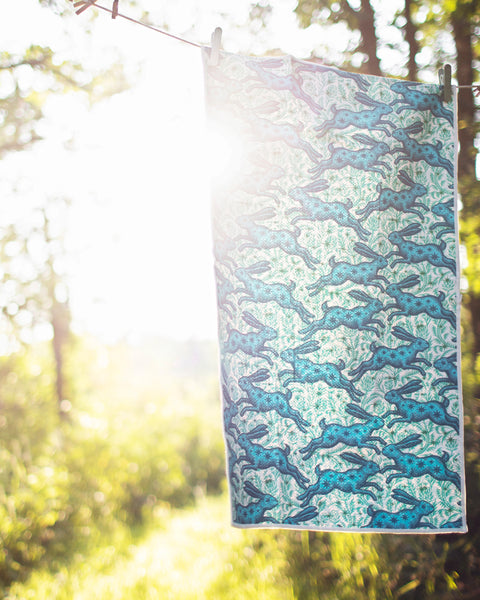 Bunnies On Parade Kitchen & Tea Towel hanging in sunlight, vibrant rabbit design, eco-friendly fabric, outdoor setting.