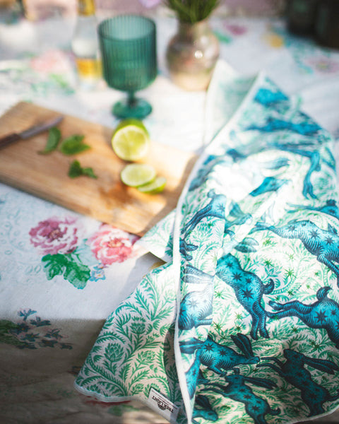 Bunnies On Parade Kitchen & Tea Towel draped on a floral table, with limes and mint on a cutting board.
