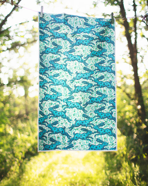 Bunnies On Parade Kitchen & Tea Towel hanging outside, featuring vibrant bunny designs on recycled fabric.