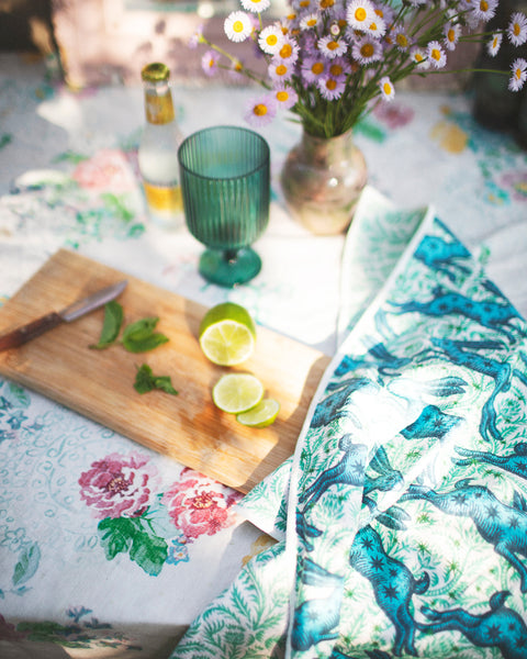 Bunnies On Parade Kitchen & Tea Towel displayed on a floral table, featuring vibrant colors and a summer setting.