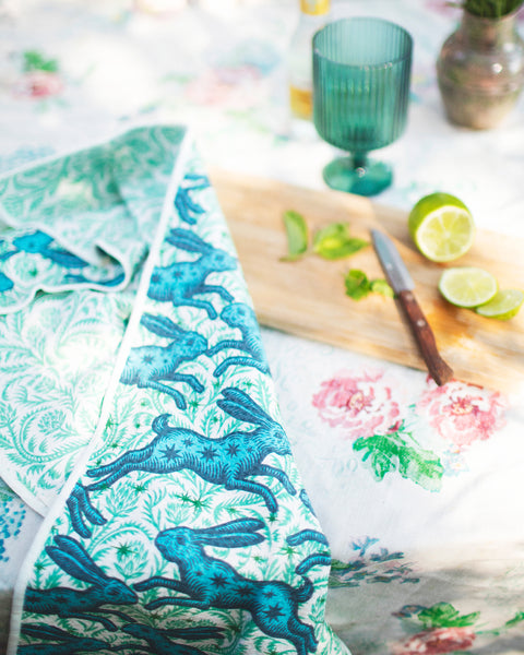 Bunnies On Parade Kitchen & Tea Towel displayed on a vibrant table with fresh limes and a drink.