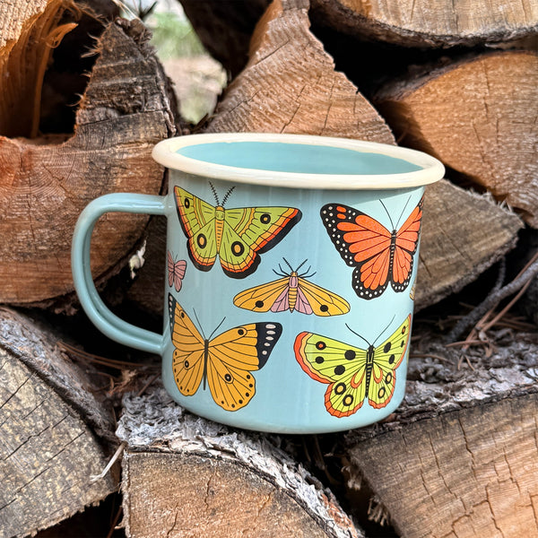 Butterfly Beauty Mug - Enamel 16oz Mug surrounded by logs, showcasing colorful butterfly designs.