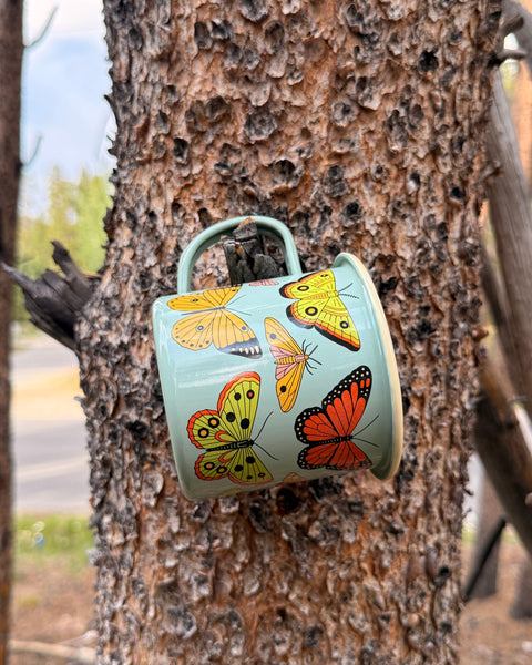 Butterfly Beauty Mug - Enamel 16oz Mug hanging on a tree, showcasing delicate butterfly designs.