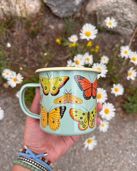 Butterfly Beauty Mug - Enamel 16oz Mug displayed outdoors with daisies and butterflies.
