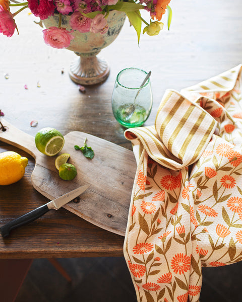 Calendula Flowers Kitchen & Tea Towel draped over a wooden cutting board with citrus fruits and a flower vase.