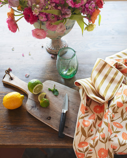 Calendula Flowers Kitchen & Tea Towel paired with fresh lemons and limes on a wooden cutting board.