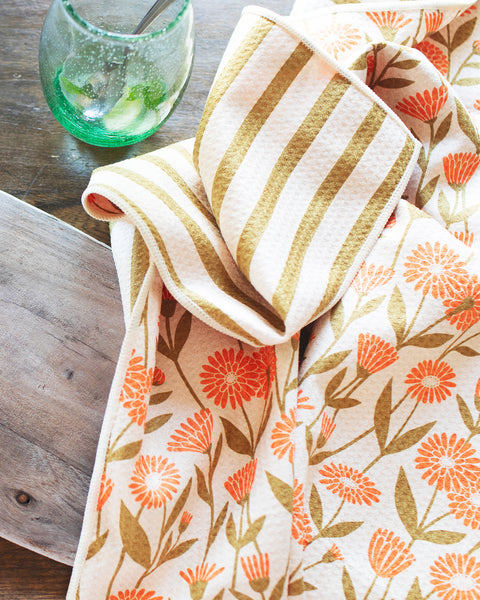 Calendula Flowers Kitchen & Tea Towel displayed with fresh fruits and a knife on a wooden cutting board.