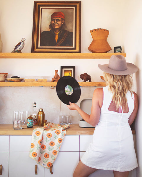 Woman holding a vinyl record in a kitchen with California Kitchen & Tea Towel draped over the counter.