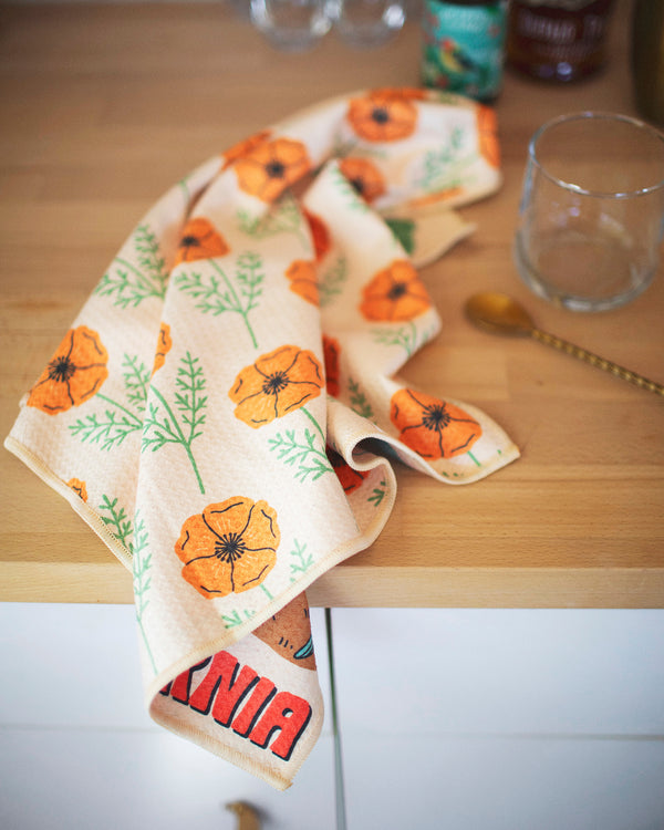 California Kitchen & Tea Towel with vibrant orange poppy design on a wooden kitchen counter.