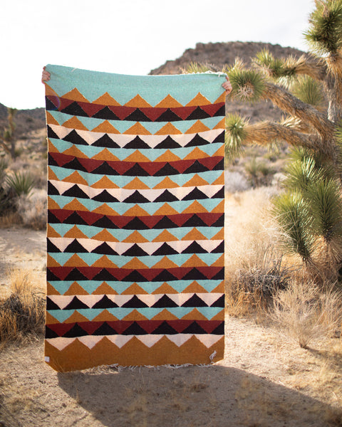 A person holding the Cascade Blanket featuring a geometric design in earthy tones, perfect for decor and outdoor use.