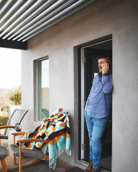 Cascade Blanket draped over a chair, offering cozy styling on a patio with a man on a phone.
