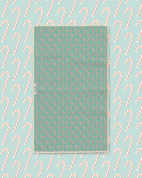 Candy cane print kitchen tea towel styled on a matching teal candy cane backdrop
