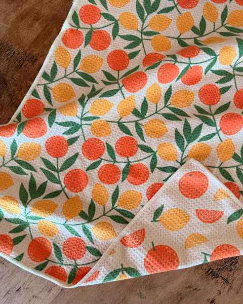 Saved By Citrus Kitchen & Tea Towel featuring a vibrant orange and yellow fruit design on absorbent fabric.