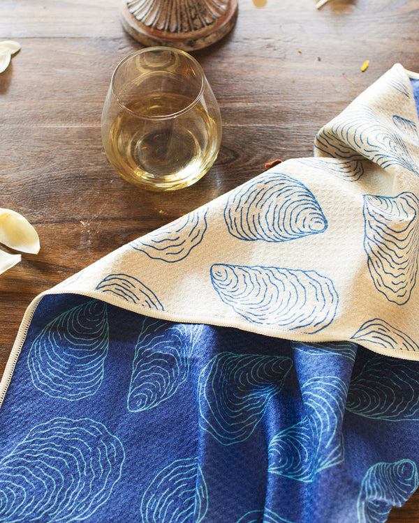 Coastal Oysters Kitchen & Tea Towel displayed on a wooden table with a glass of white wine.