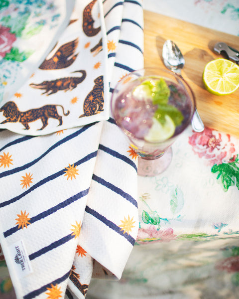 Cosmic Creatures Kitchen & Tea Towel draped over a table with a drink and sliced lime.