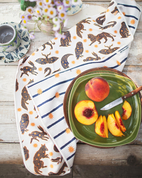 Cosmic Creatures Kitchen & Tea Towel displayed with fresh peaches on a rustic wooden table.