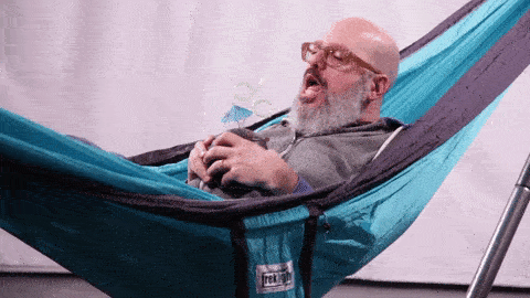 Man relaxing in a Trek Light hammock, sipping a drink and enjoying leisure time.
