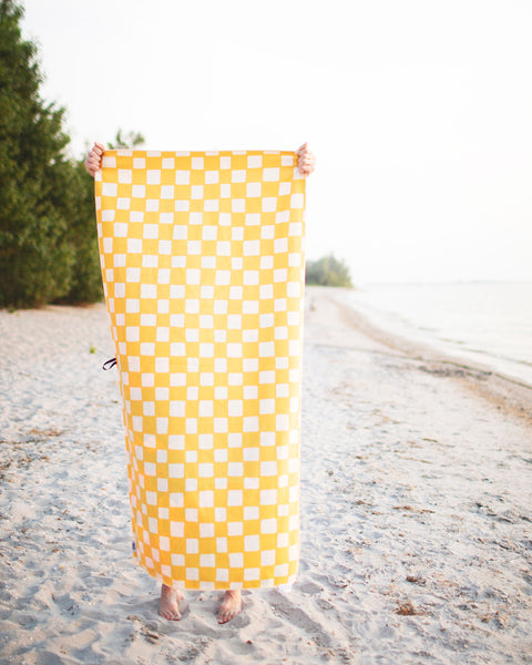 Desert Dreams Wander & Travel Towel in a vibrant yellow checkered design at the beach, perfect for your travels.