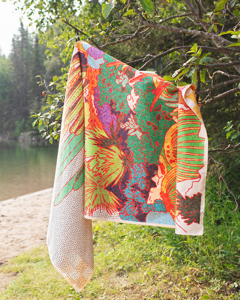 Desert Dreams Wander & Travel Towel hanging by a lake, showcasing vibrant colors and patterns, perfect for travel.