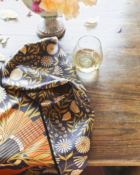 Dinner Music Kitchen & Tea Towel draped on a table, surrounded by flowers and a glass of wine.