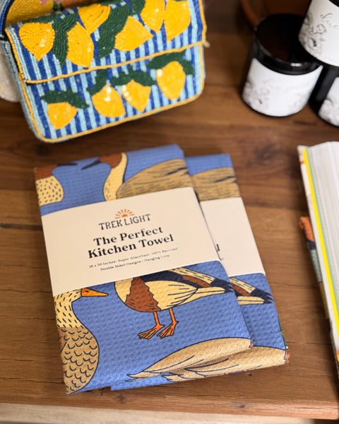Ducks In A Row Kitchen & Tea Towel displayed on a wooden table with vibrant designs and packaging.