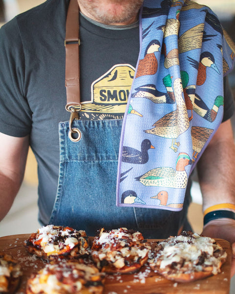 Ducks In A Row Kitchen & Tea Towel displayed on a shoulder while cooking dishes, showcasing its vibrant design.