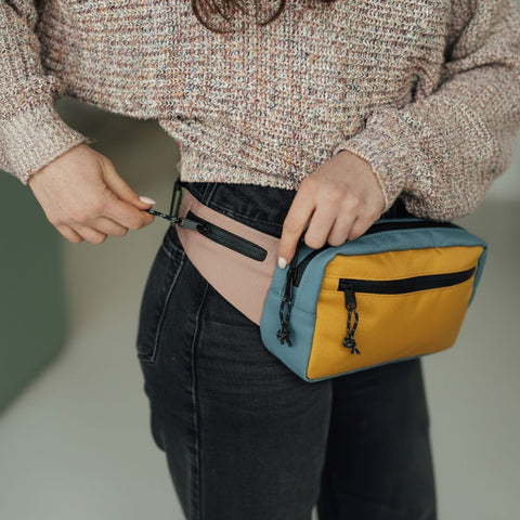 Person wearing a stylish fanny pack and sweater, adjusting the zipper on their jeans. Trendy fashion accessory.
